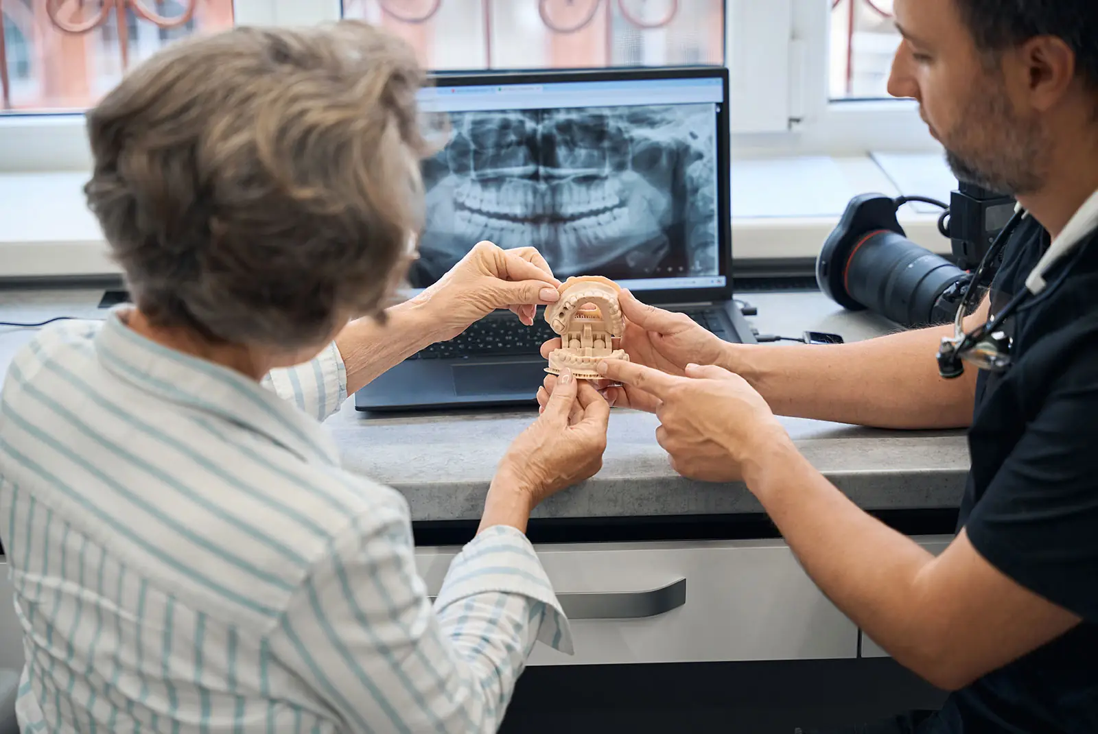 Dentist reviewing a dental model and panoramic X-ray with a patient